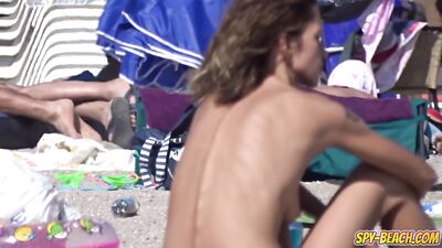 A gorgeous girl sunbathes topless on the beach
